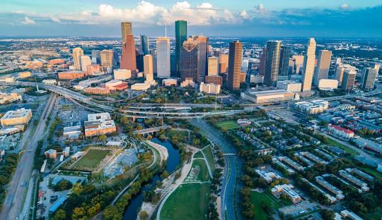Aerial view of Houston skyline with modern skyscrapers, green parks, and winding waterways, showcasing the vibrant urban landscape of Harris County, Texas.