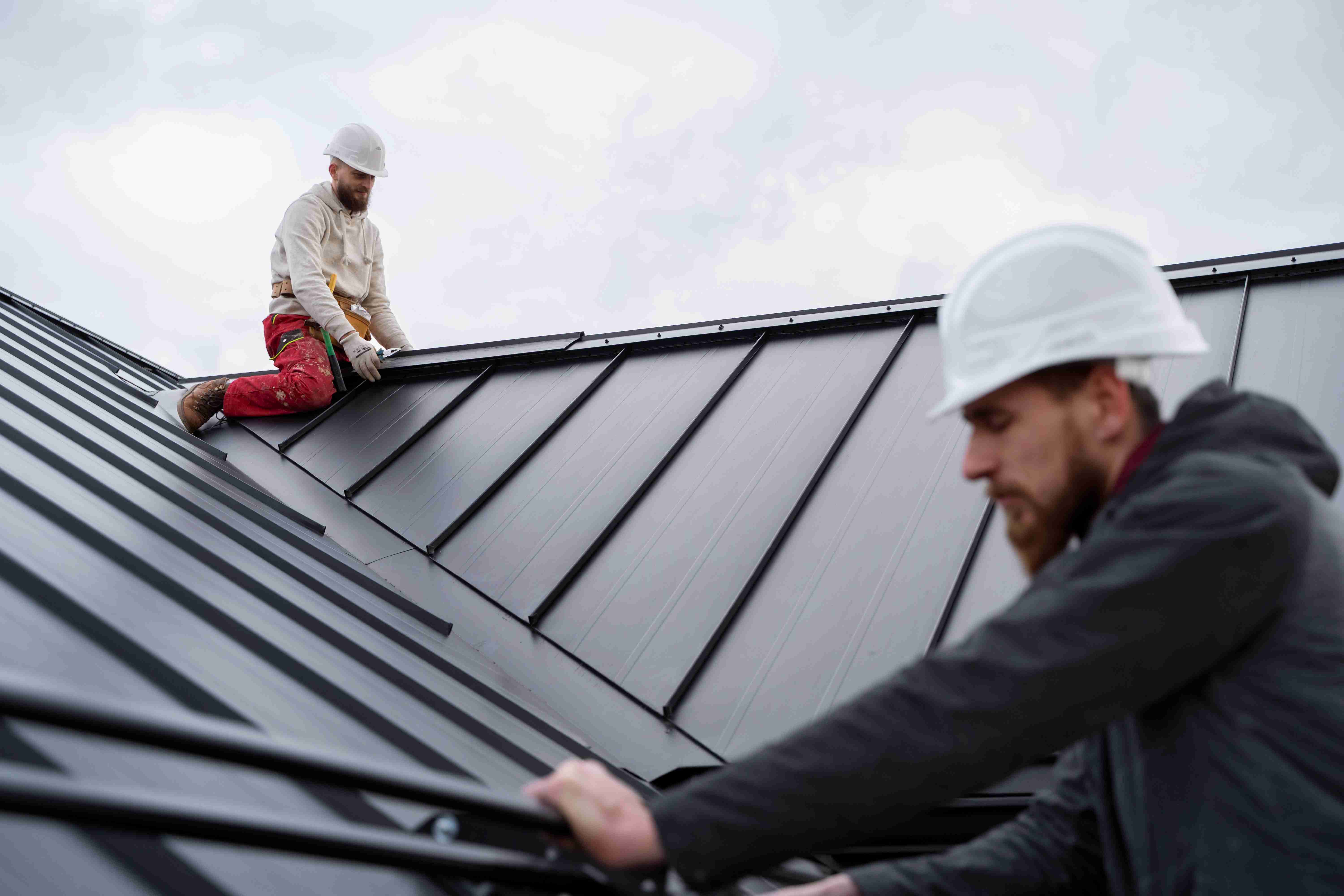 Men installing a metal roof, showcasing professional craftsmanship and teamwork in a residential setting, emphasizing durability and quality in roofing services.