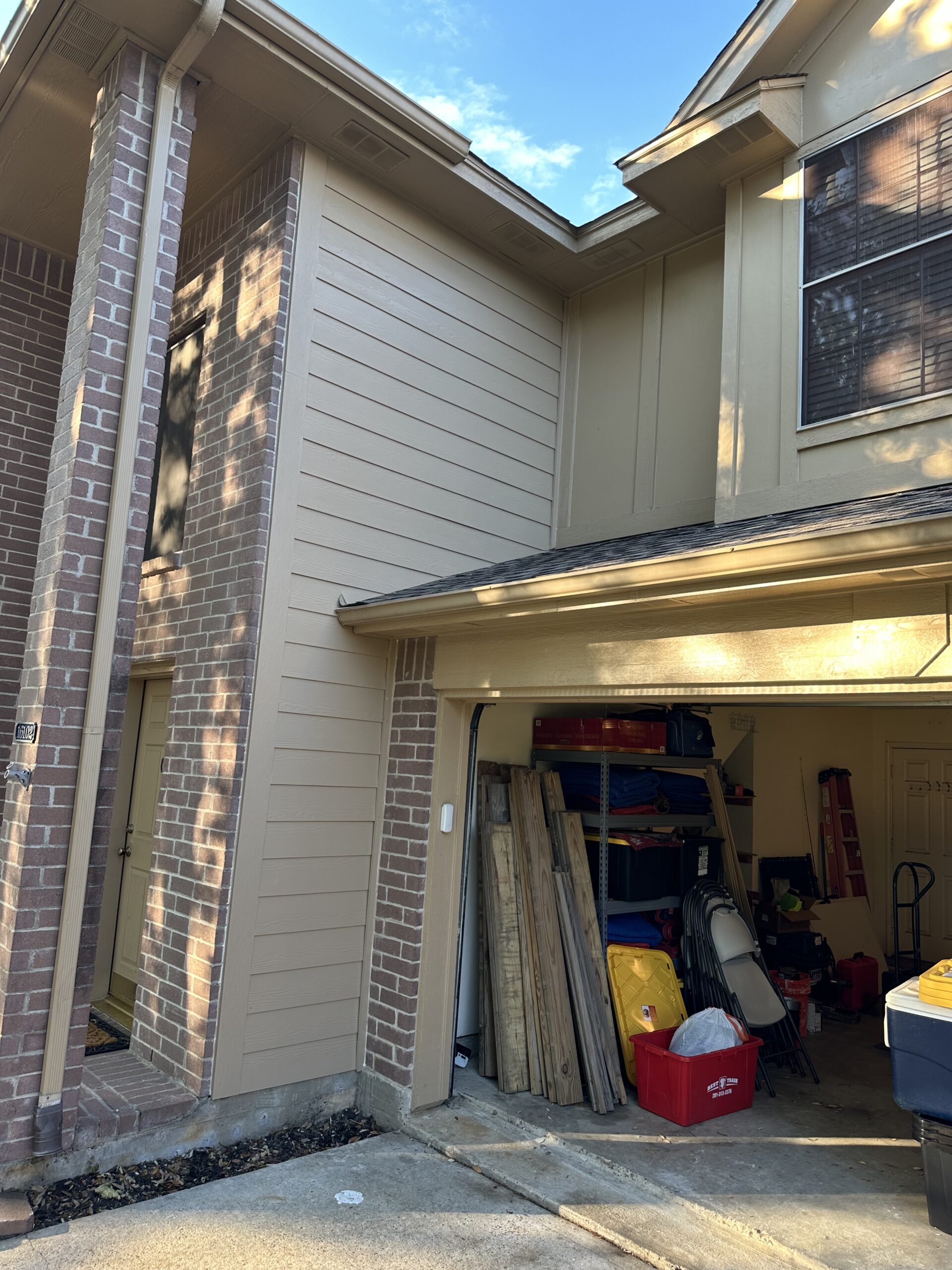 Exterior view of a residential property showcasing new siding and brickwork, emphasizing quality craftsmanship by Tekton Exteriors in Texas, with a garage partially visible filled with construction materials.