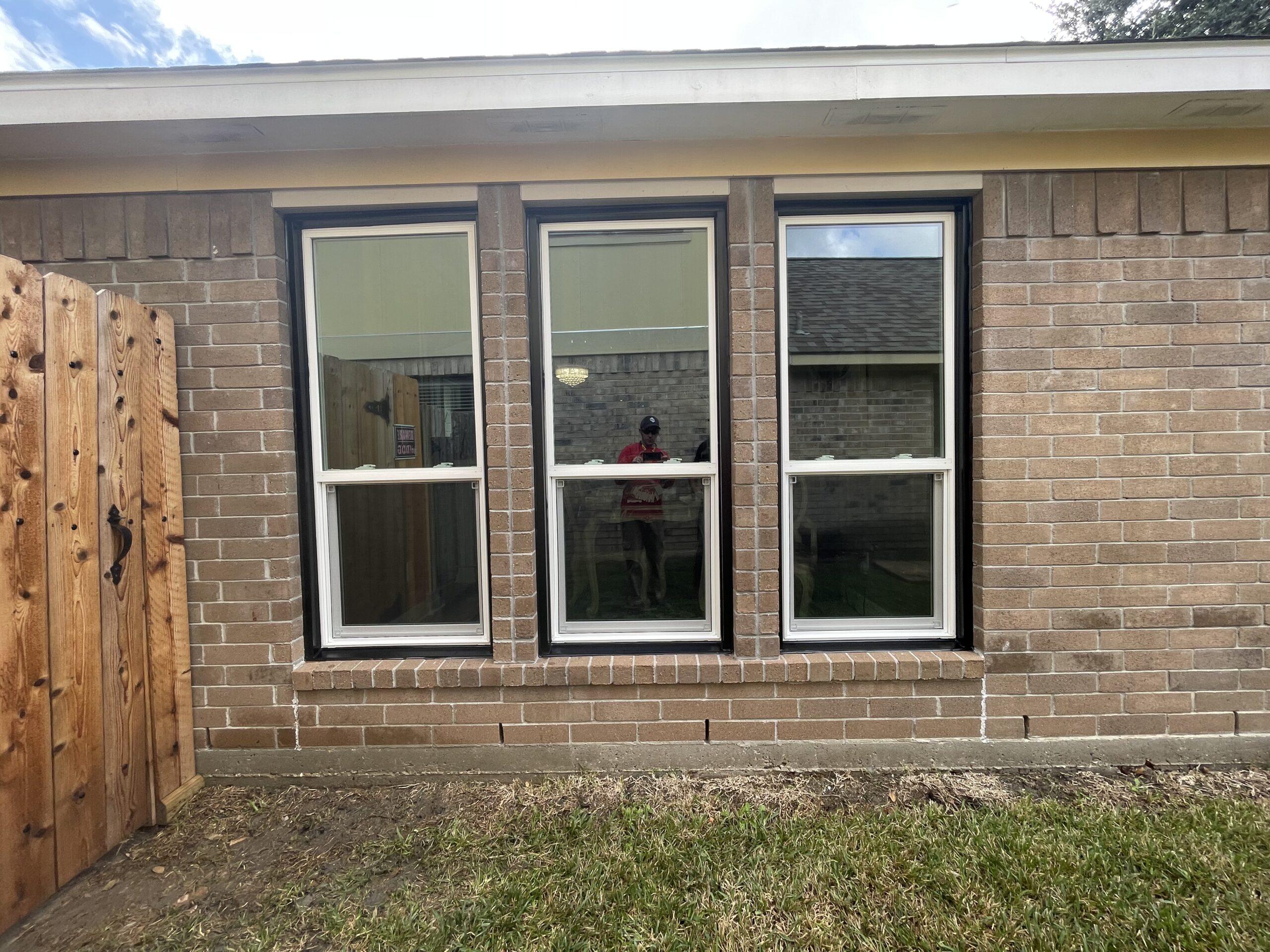 Newly installed double-pane windows with black frames on a brick exterior wall, showcasing quality craftsmanship by Tekton Exteriors in a residential setting.