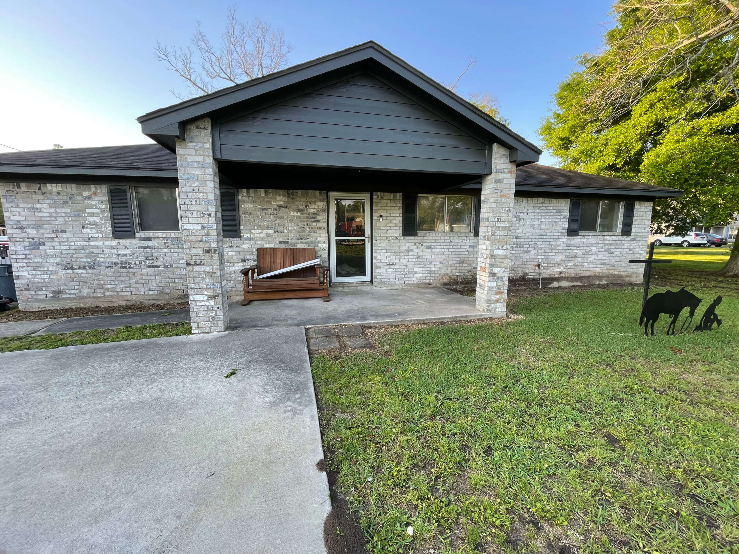 Front view of a remodeled home featuring a modern gray facade, a wooden bench on the porch, and decorative metal silhouettes of animals in the yard, highlighting Tekton Exteriors' home improvement services.