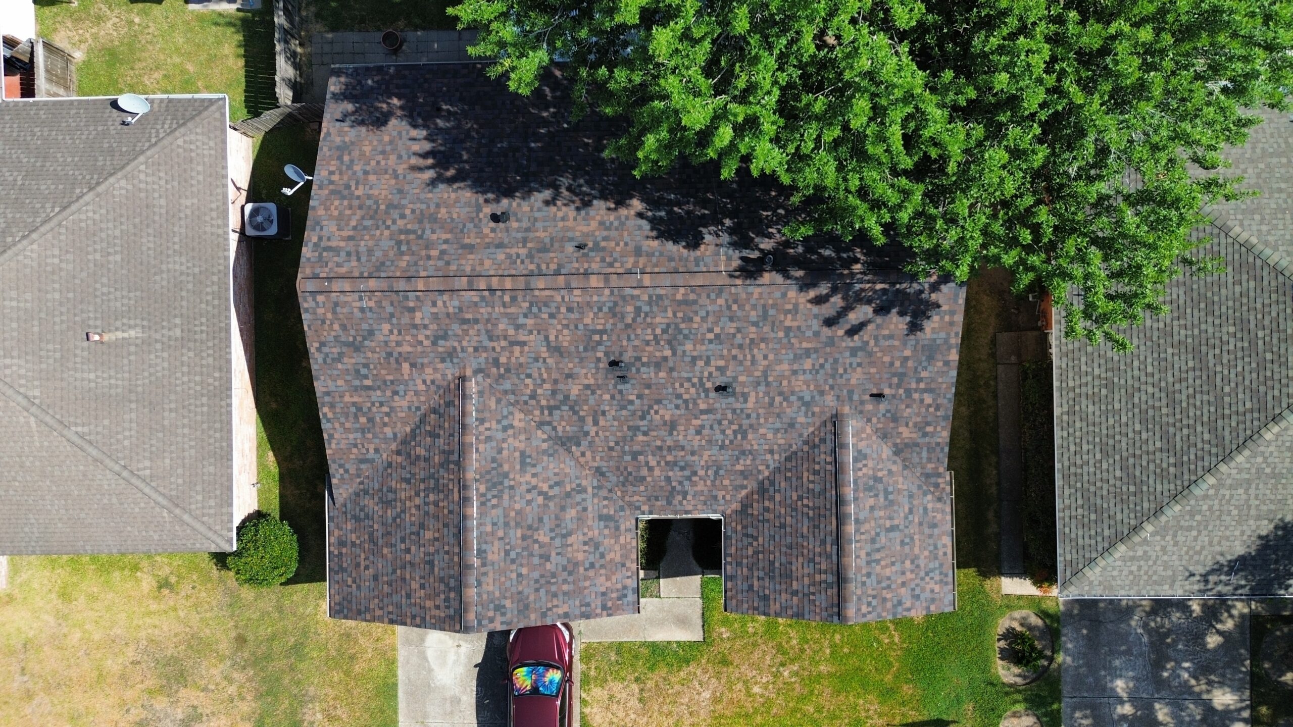 Aerial view of a newly installed roof featuring textured shingles, surrounded by residential homes and green landscaping, showcasing Tekton Exteriors' quality craftsmanship in roofing services.